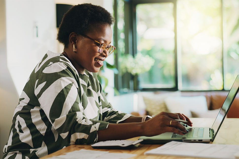 Happy African American woman sitting at desk working on laptop.