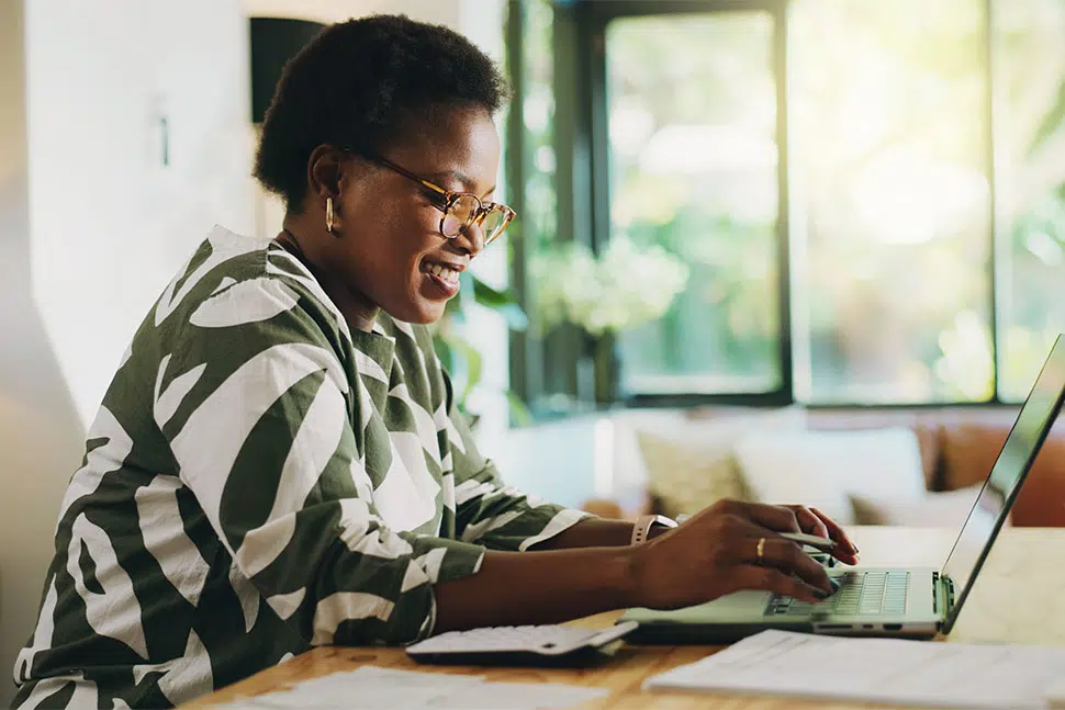Happy African American woman sitting at desk working on laptop.
