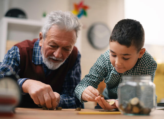 Grandfather and grandson counting money for piggy bank