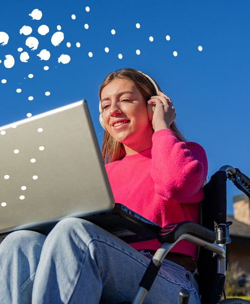 Woman in wheelchair using headphone and looking down at laptop smiling