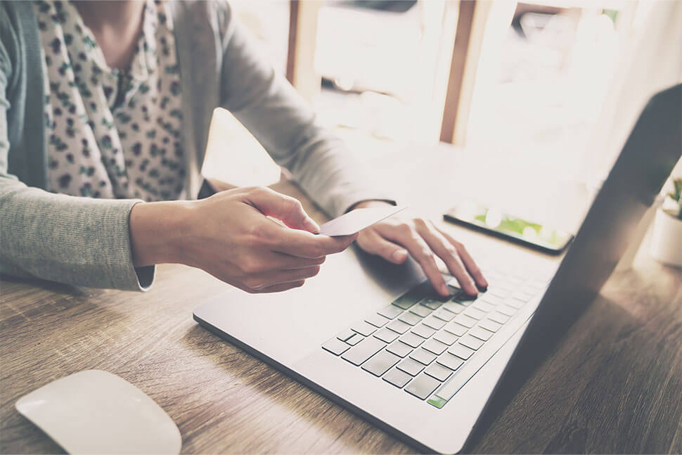 Woman sitting at desk with one hand holding a credit card and other hand on keyboard of laptop.