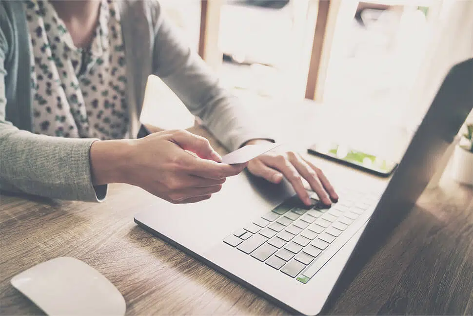 Woman sitting at desk with one hand holding a credit card and other hand on keyboard of laptop.