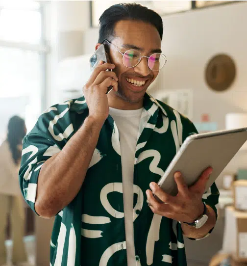 Man with phone up to ear smiling with tablet in other hand