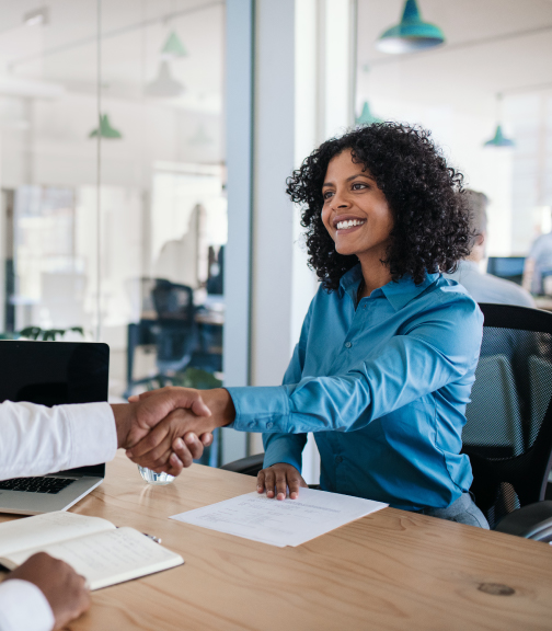 Woman sitting at conference table shaking hands with man in front of her