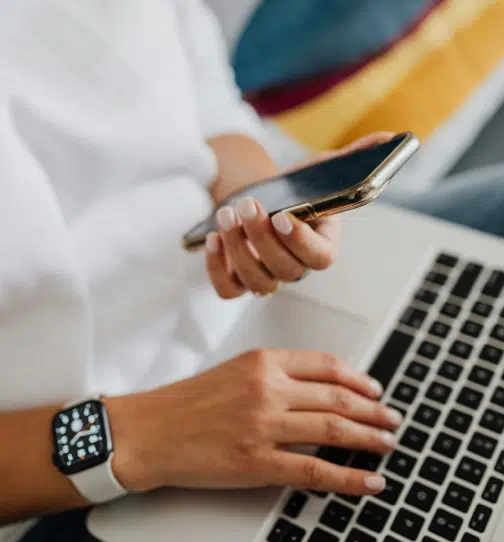 Person sitting with laptop on lap and cell phone in hand