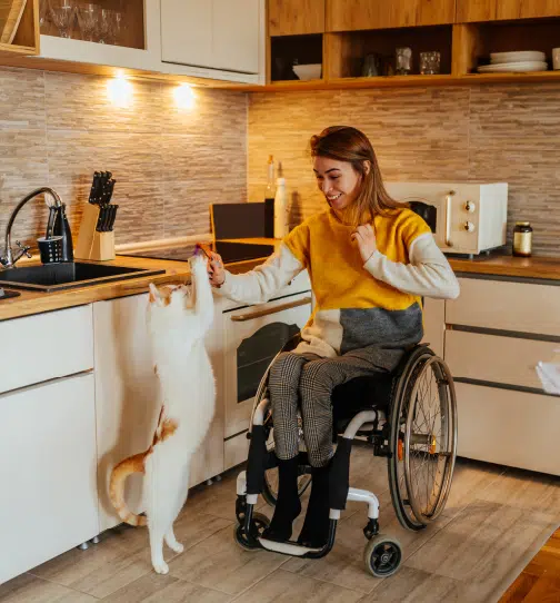 Woman in wheelchair sitting in kitchen playing with cat