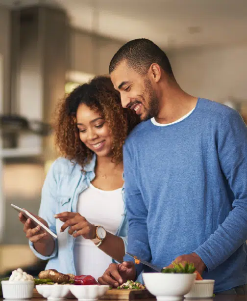 Couple looking at tablet together in kitchen with ingredients spread out in front of them