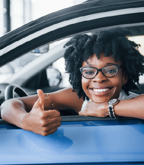Woman smiling and holding thumbs up out of car window