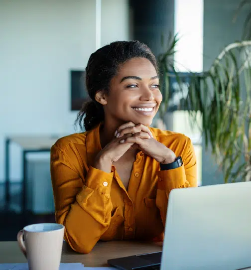 Woman sitting at desk smiling with laptop and coffee cup in front of her