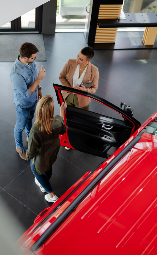 Couple talking with salesperson while standing next to red car