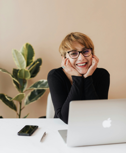 Happy woman with head in hands resting on desk with laptop in front of her