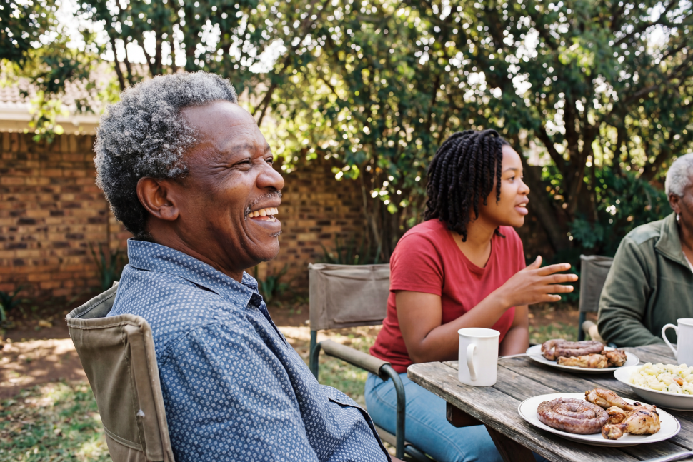 Image of an older gentleman - grandpa - smiling and sitting at an outdoor table with family. Family picnic.